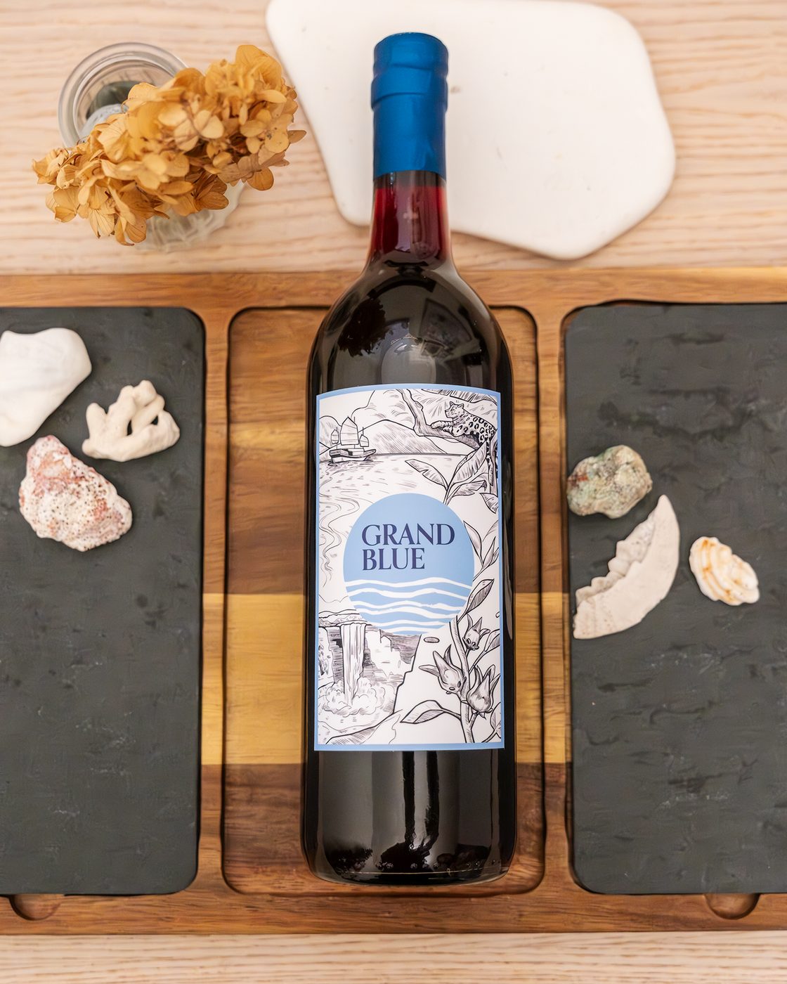 Grand Blue Sorrel bottle centered on a wooden board with shells and dried flowers