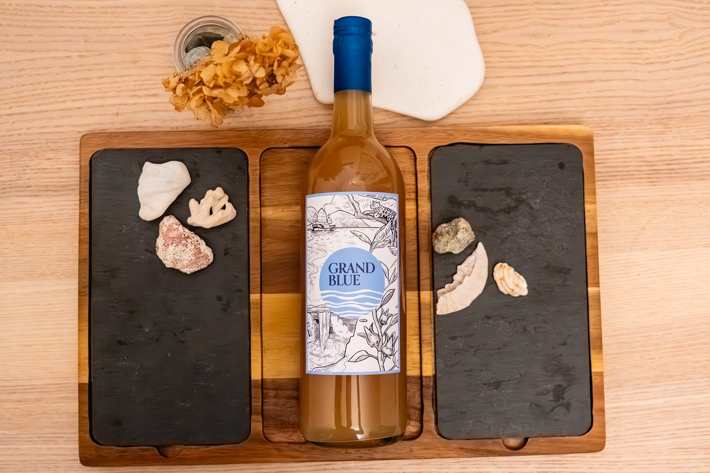Grand Blue Ginger Beer bottle centered on a wooden board with shells and dried flowers