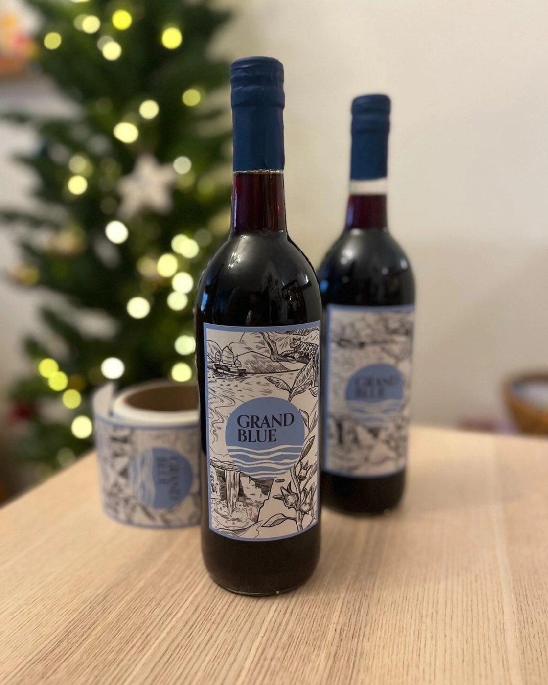Two Grand Blue Sorrel bottles beside warm Christmas tree lights
